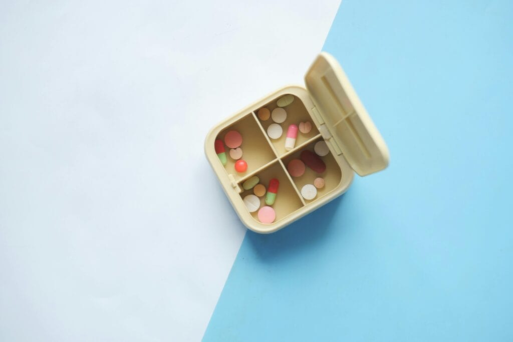 Top view of an open pill box filled with various pills and capsules on a blue and white background.